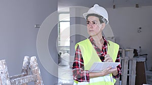 Portrait of excited young woman builder next to stepladder with documents in her hands checks quality of completed