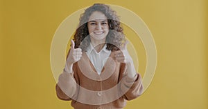 Portrait of excited young woman smiling with thumbs-up hand gesture on yellow color background