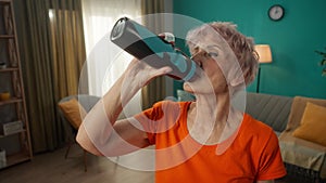 Portrait of an exhausted grayhaired elderly woman after a workout in the living room. Tired elderly woman drinks water