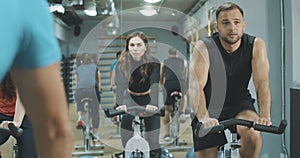 Portrait of exhausted men and women riding cycling equipment in gym. Front view of perspiring athletic people training