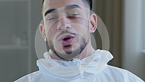 Portrait of exhausted tired young arab male doctor nurse practitioner in protective uniform latex gloves stands in