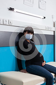 Portrait of expectant adult sitting on bed in medical cabinet