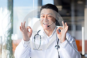 Portrait of an experienced Asian doctor, looking at the camera and having fun talking to the patient, smiling amicably and