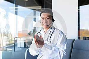 Portrait of an experienced Asian doctor, looking at the camera and having fun talking to the patient, smiling amicably and