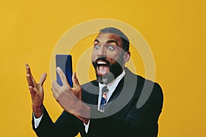 portrait of expressive angry excited bearded man in suit and tie with smartphone video call hand up yellow background