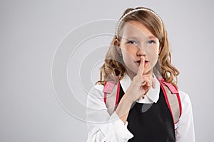 Portrait of an expressive, beautiful young schoolgirl girl who put her finger to her lips to create a gesture of silence and atten