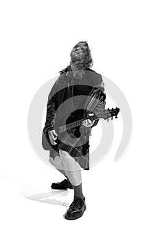 Portrait of expressive young man with long hair, rock musician playing guitar over white background. Black and white