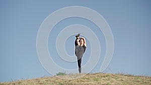 Portrait of extremely flexible young woman raising leg up. Wide shot of Caucasian sportswoman warming up outdoors