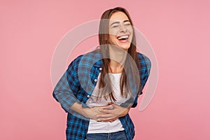 Portrait of extremely happy girl in checkered shirt holding her stomach and laughing out loud, chuckling giggling