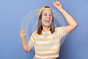 Portrait of extremely happy joyful teenager girl wearing baseball cap and stripe T-shirt posing isolated over blue background,