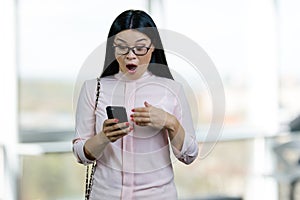 Portrait of extremely surprised asian woman looking at her smartphone.