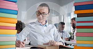 Portrait f young woman in glasses reading book and taking notes studying in classroom