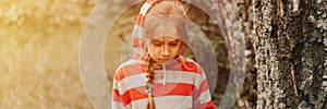 Portrait face of upset or focused thoughtful scowl eight year old kid girl in hood of striped hoodie in the forest nature. prepube