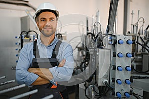 Portrait of factory worker in protective uniform and hardhat standing by industrial machine at production line. People