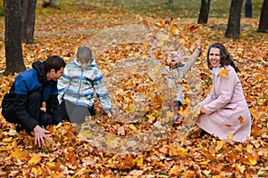 Portrait of a family in an autumn park. Happy people playing with fallen yellow leaves