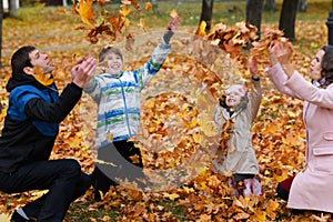 Portrait of a family in an autumn park. Happy people playing with fallen yellow leaves