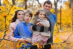 Portrait of a family in an autumn park. Happy people pose against the background of beautiful yellow trees. They hug and are happy