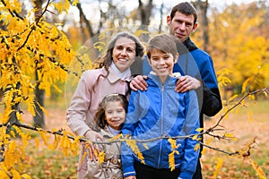 Portrait of a family in an autumn park. Happy people pose against the background of beautiful yellow trees. They hug and are happy