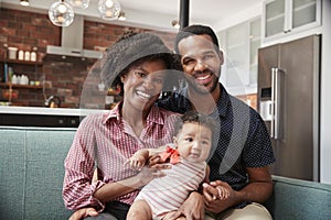 Portrait Of Family With Baby Daughter Relaxing On Sofa At Home Together