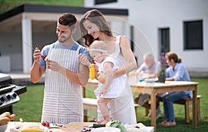 Portrait of family with baby outdoors on garden barbecue, grilling.