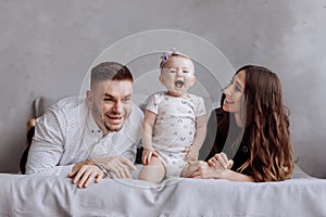Portrait of a family on the bed at home while playing with their baby girl - Father, mother and one year old little daughter have