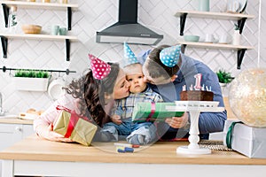 Portrait of a family celebrating birthday of their little baby boy, kissing baby. Family fun concept, first birthday