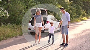 Portrait of a family with a child near a car with an open trunk on an empty road