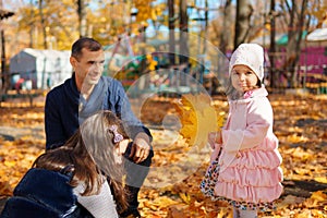 portrait of a family with children in an autumn city park, happy people walking together, playing with yellow leaves, beautiful
