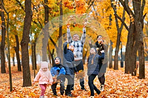 Portrait of a family with children in an autumn city park - happy people walking together, they toss the leaves, beautiful nature