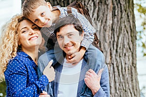 Portrait of family: mother, father and boy, son with satchel hugging his mom while sitting on father`s shoulders