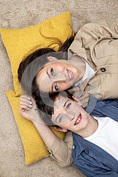 Portrait of a family, a mother and a teenage son lying on pillows, hugging, looking at the camera, smiling. Close-up