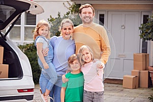 Portrait Of Family Outside New Home On Moving Day Unloading Boxes From Car