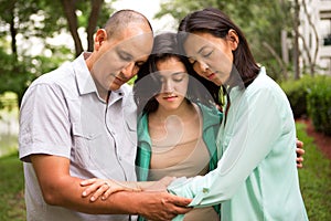 Portrait of a family praying with their daughter.