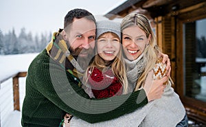 Portrait of family with small daughter outdoors in winter holiday cottage, looking at camera.