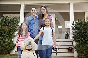 Portrait Of Family Standing in Front Of House With Pet Dog