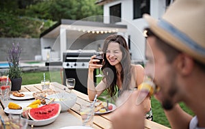 Portrait of family with wine sitting at table outdoors on garden barbecue.