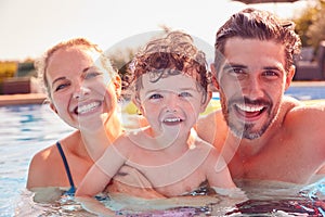 Portrait Of Family With Young Son Having Fun On Summer Vacation In Outdoor Swimming Pool