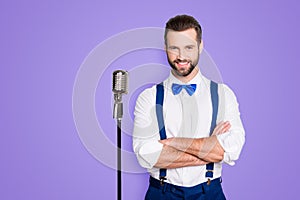 Portrait of famous joyful singer with bristle, wearing blue pants bowtie suspenders shirt, having his arms crossed