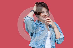 Portrait of fancy beautiful brunette young woman with makeup in denim casual style standing holding her hair and looking at camera