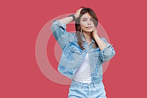 Portrait of fancy beautiful brunette young woman with makeup in denim casual style standing, posing with hands on head and looking