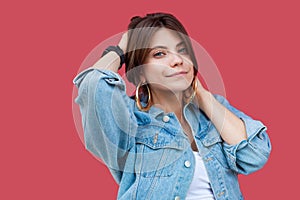 Portrait of fancy beautiful brunette young woman with makeup in denim casual style standing, posing with hands on head and looking