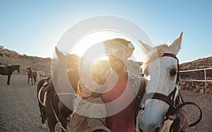 Portrait of farmer couple having fun doing selfie with bitless horses at ranch corral - Soft focus on left animal eye