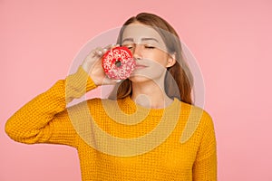 Portrait of fascinating hungry ginger girl in sweater smelling doughnut and expressing desire to eat sweet donut