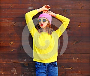 Portrait fashion cool girl in colorful clothes over wooden background wearing pink hat yellow sweater
