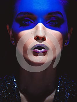 Portrait of fashion girl with stylish makeup and blue neon light on her face on the black background in the studio