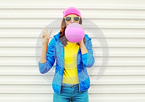 Portrait fashion pretty cool girl blowing pink air balloon in colorful clothes having fun over white background wearing a pink hat