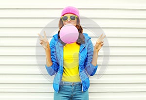 Portrait of fashion pretty cool girl blowing pink air balloon in colorful clothes having fun over white wearing a pink hat