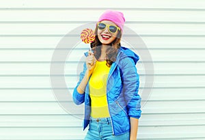 Portrait fashion pretty cool smiling woman with lollipop in colorful clothes over white background, wearing a pink hat