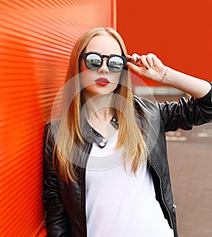 Portrait fashion pretty woman wearing a rock black leather jacket and sunglasses in city over red