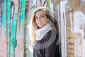 Portrait, fashion and smile of woman at graffiti wall in city outdoor for street art. Face, winter style and happy, gen